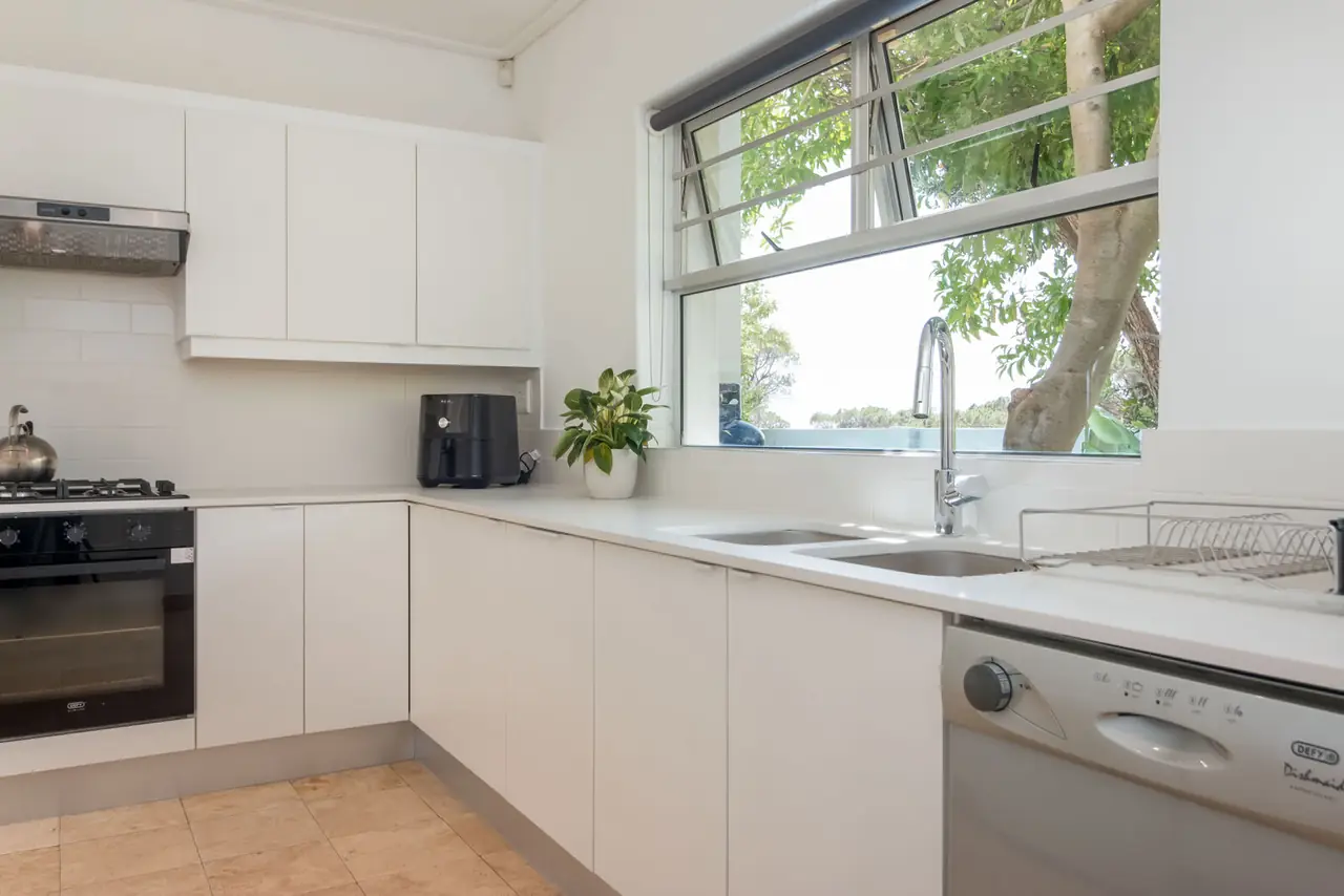 White kitchen with double sink under a window onto the trees